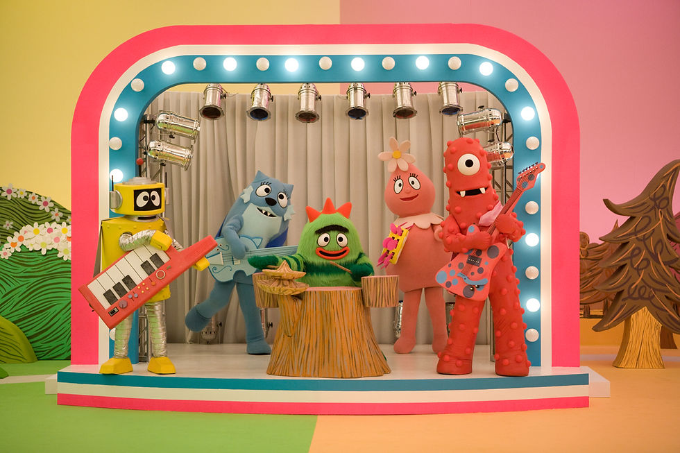 Colorful characters in a band perform on a vibrant stage with lights. They play instruments amid a playful backdrop of trees and hills.