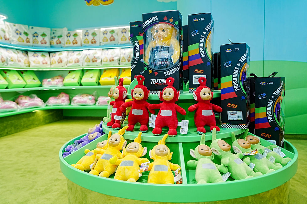 Colorful store display of Teletubbies plush toys and boxed figures, with red, yellow, green, and purple characters on green shelves