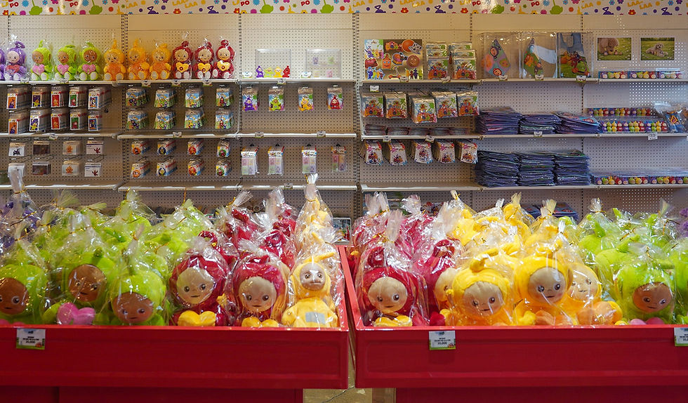 Colorful stuffed toys in plastic wrap on red shelves in a store. Background displays additional toys and books. Bright, cheerful setting.