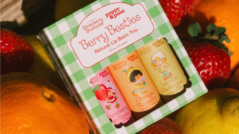 Poppy & Pout Berry Besties natural lip balm trio in a green checkered box among strawberries and oranges, with Strawberry, Orange, Lemon labels.