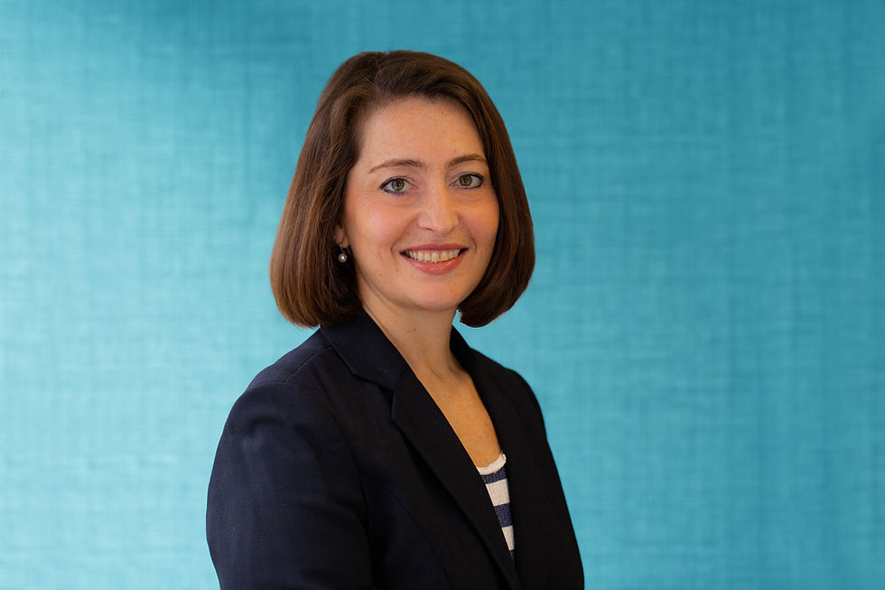 a woman in a jacket and stripped shirt poses in front of a blue wall