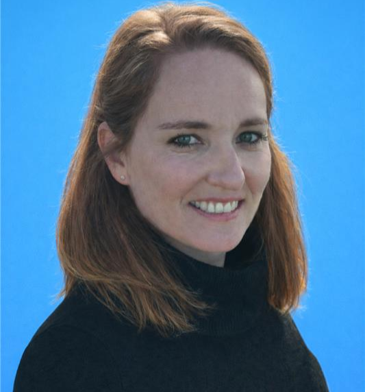 Photo of Marie Kopp - a white woman with reddish brown hair, wearing a black turtleneck against a blue background