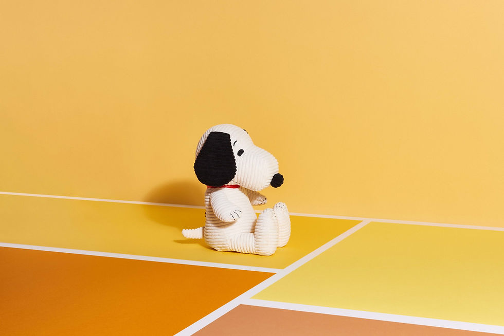 A plush Snoopy beagle toy sits on a yellow background.