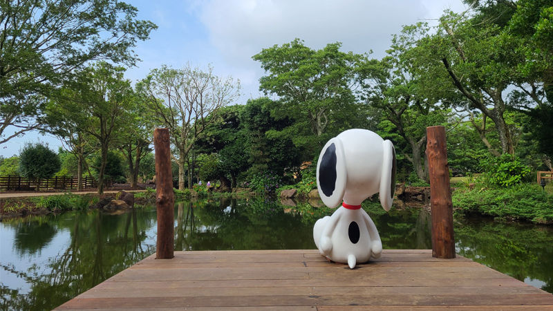 a toy beagle dog is sitting on the edge of the dock by the pond