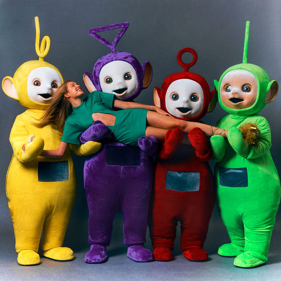 Four colourful aliens hold a model in a green dress lying across them.
