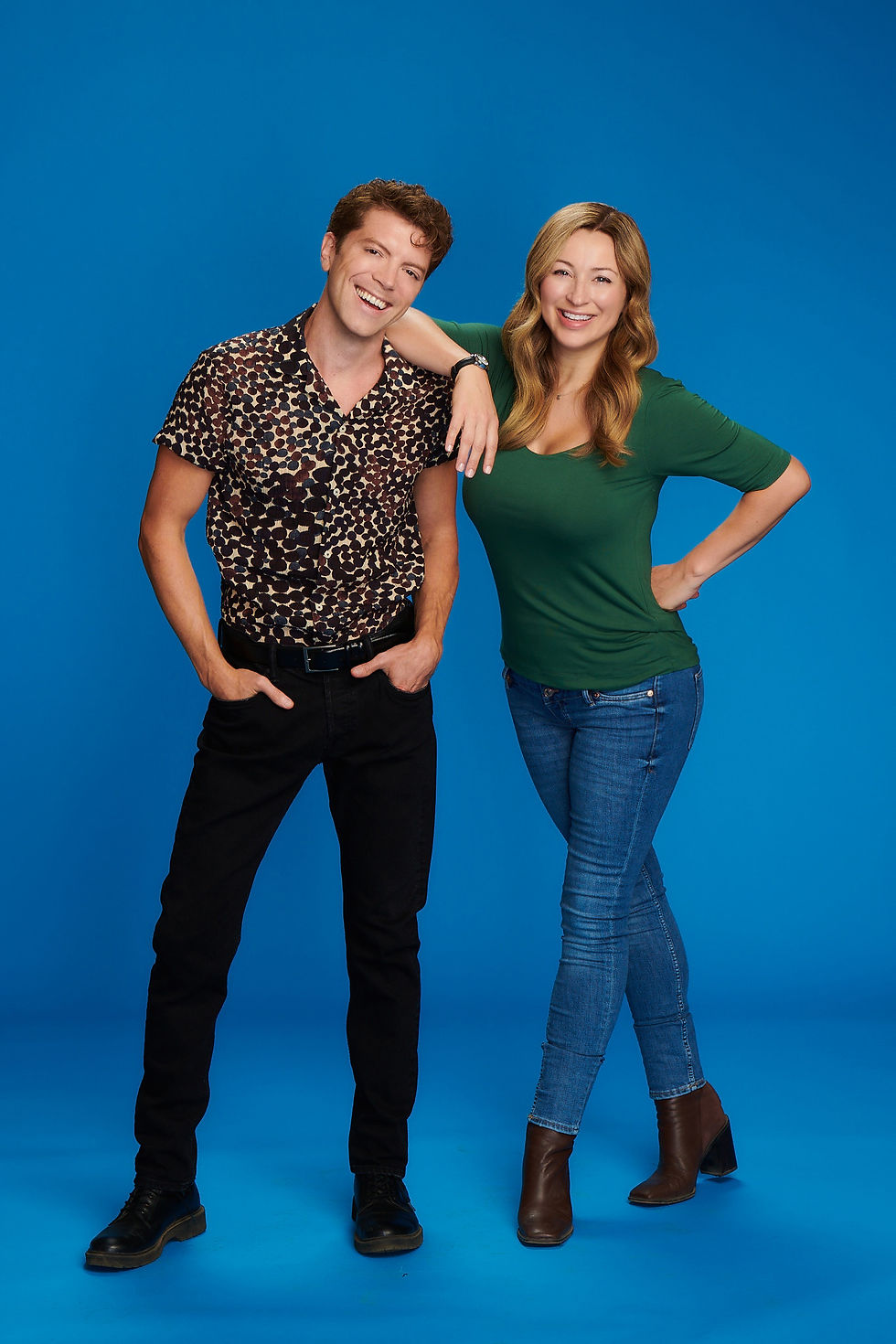 A smiling man and woman lean on each other, posing for the camera on a blue background.