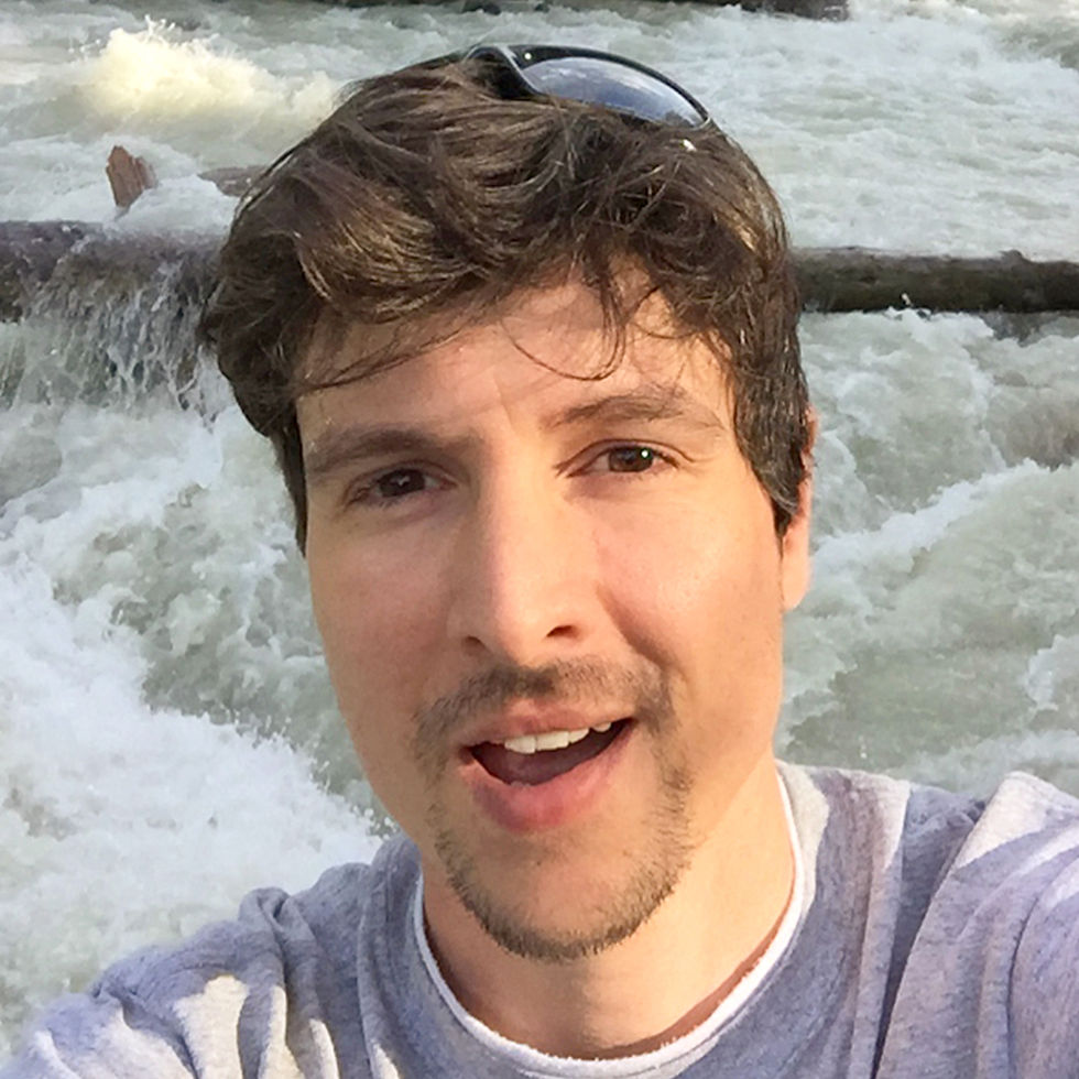close up of a brown haired person standing front of rushing rapid posing for a photo