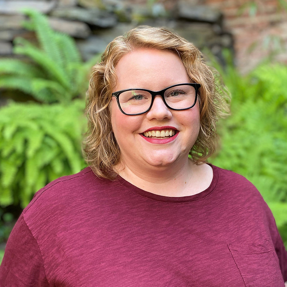 close up of a blond woman wearing glassess standing in front of some plants posing for a photo