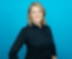 A headshot of a woman in a black shirt smiling and standing in front a blue background.