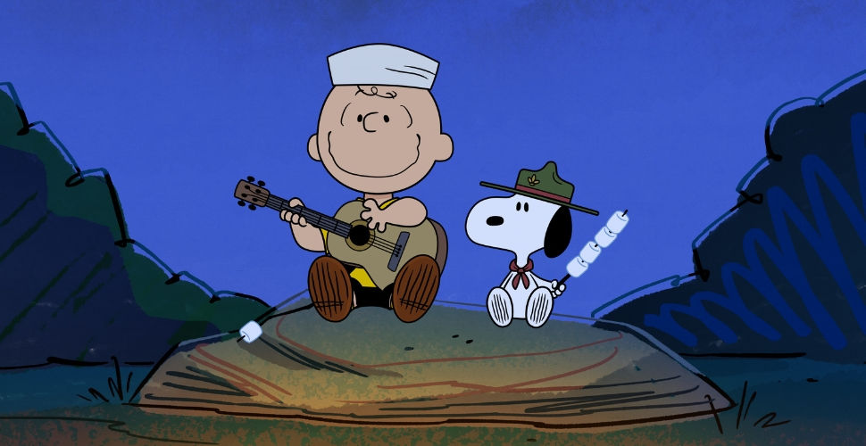 Charlie Brown playing an acoustic guitar and sitting on a big rock beside Snoopy who is wearing a ranger hat and holding marshmallows on a stick. 