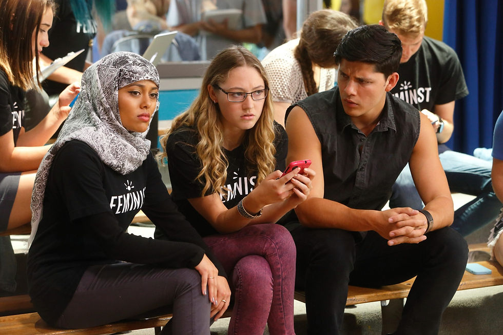three students sitting on a bench looking at a cell phone