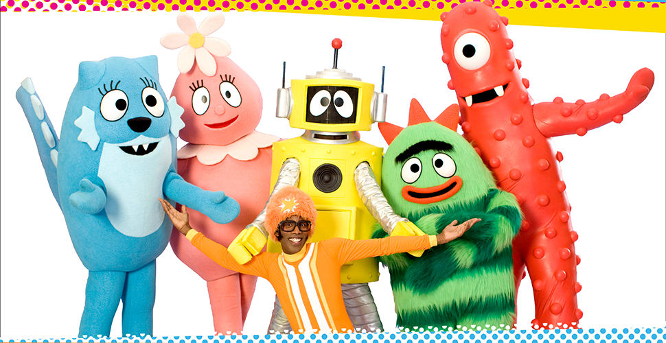 black man in an orange outfit in front of a group of colourful characters