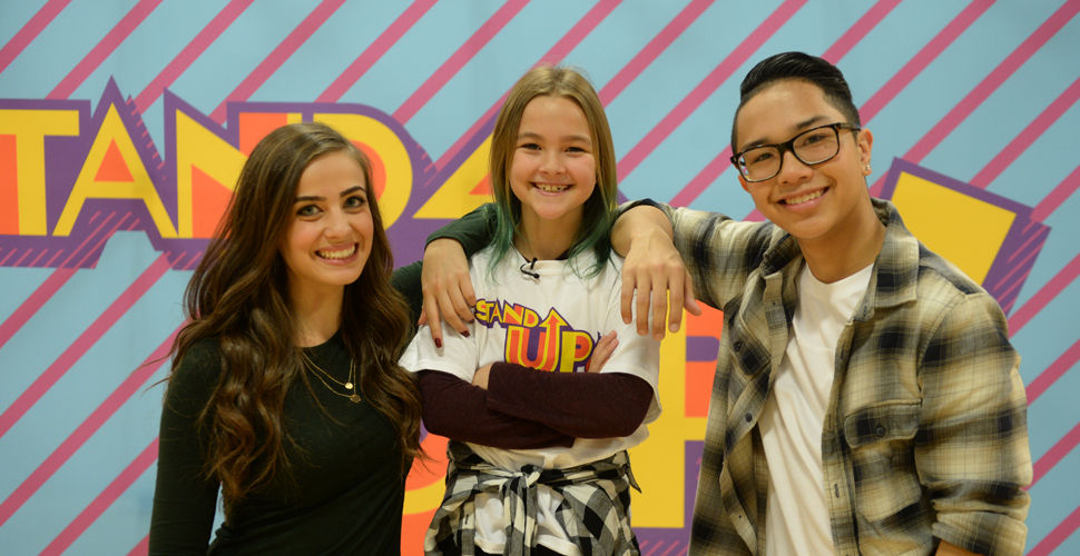 a young man and woman rest their arms on a girl wearing a Stand Up tshirt