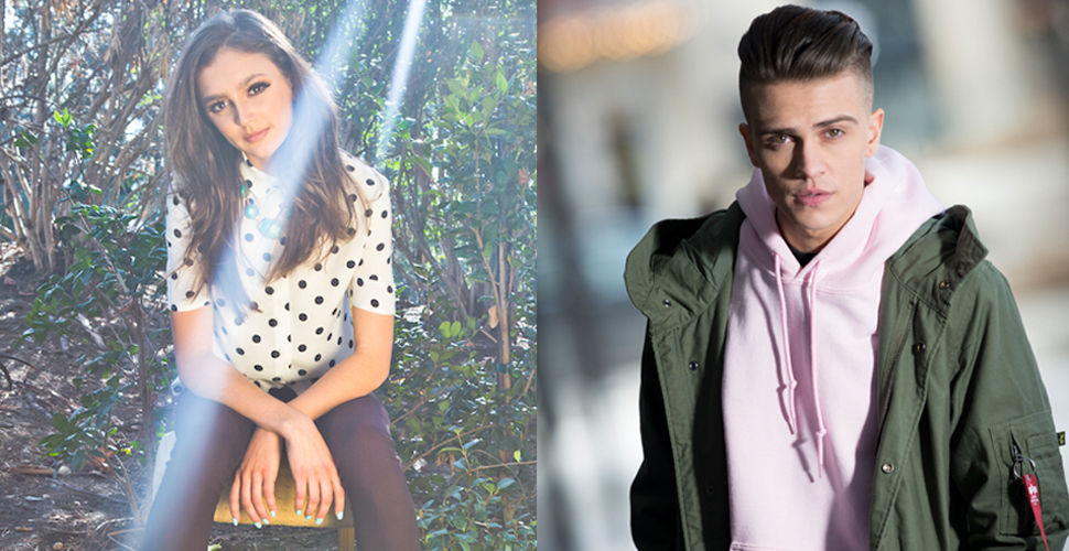 a young woman sitting in a forest with light streaming down. a young man in a pink hoodie and green jacket