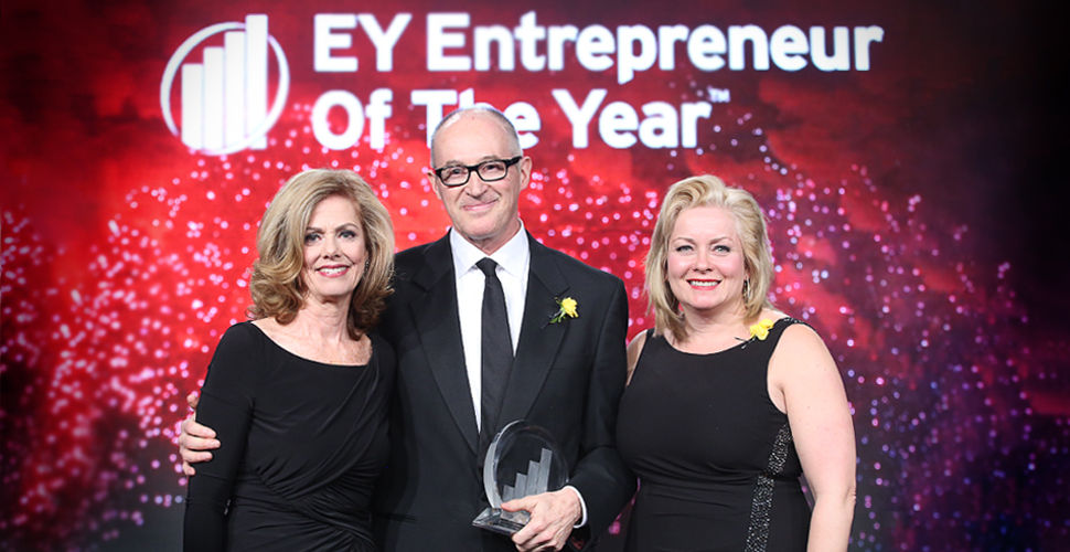 a man in a suit stands betwee two women in black dresses