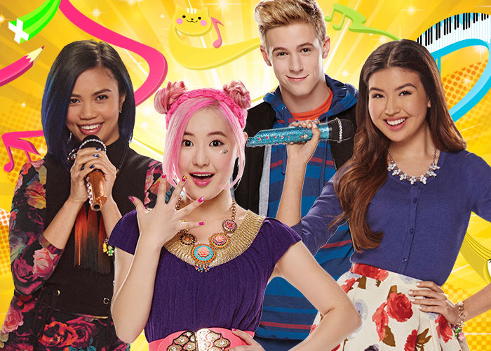 3 teenage girls and a teenage boy holding microphones in front of a colourful background.