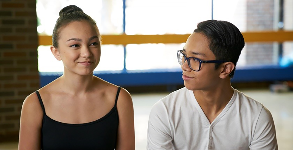 a young woman and young man look at each other in a high school dance studio