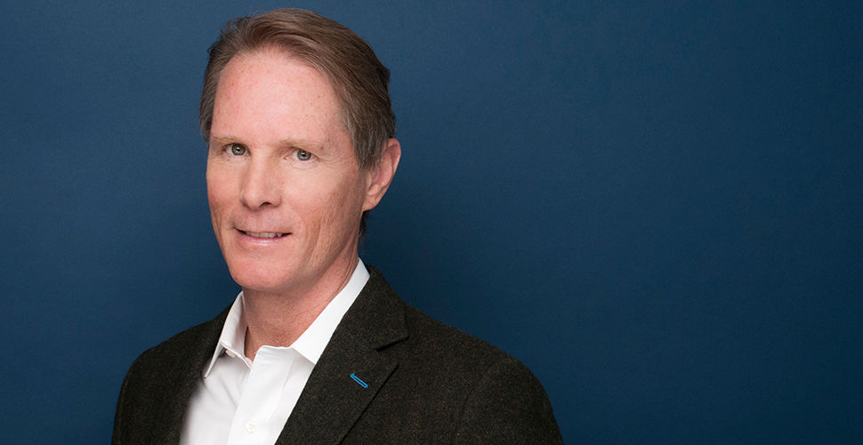 a man in a collared shirt and black jacket against a blue background